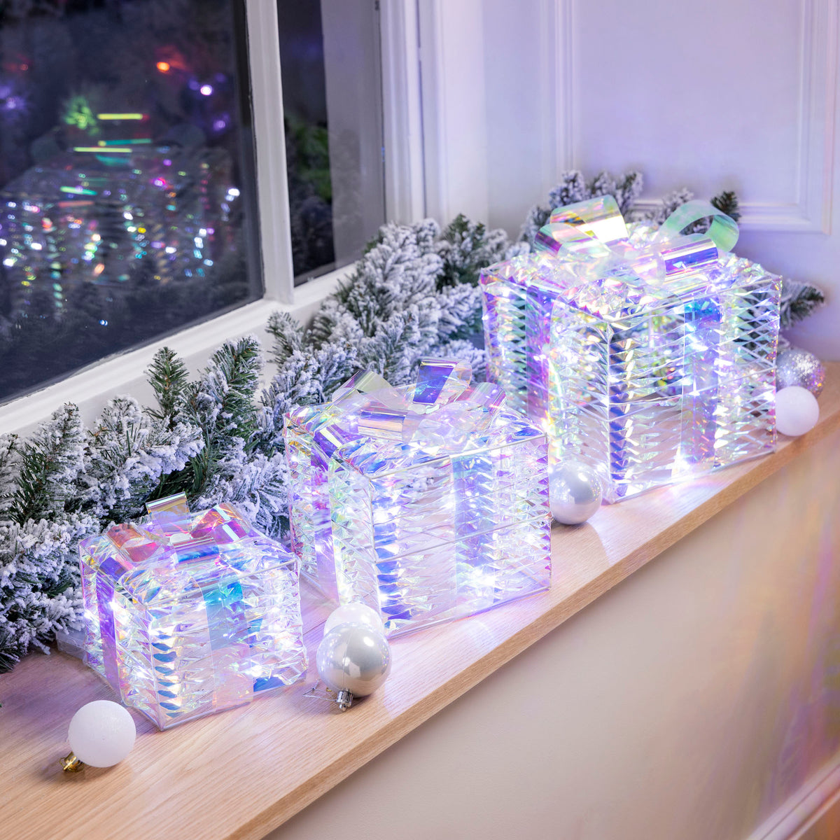 Christow Light Up Iridescent Christmas Presents displayed on a windowsill with a frosted garland