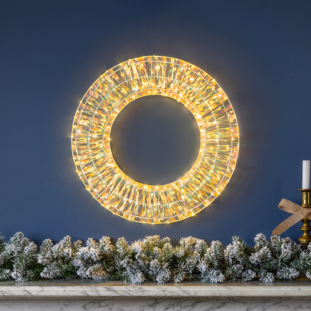 Illuminated Christow Iridescent Warm White LED Christmas Wreath displayed above a mantelpiece