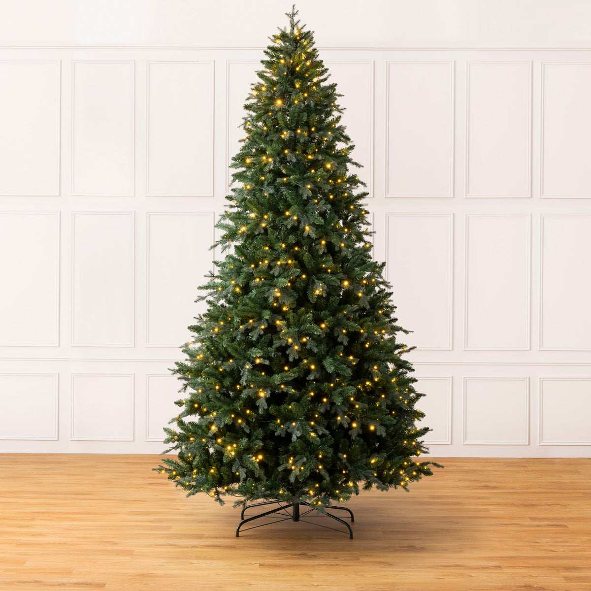 Christow Pre-Lit 10ft Fraser Fir Artificial Christmas Tree undecorated with warm white LED lights on a black metal stand against a white panelled wall