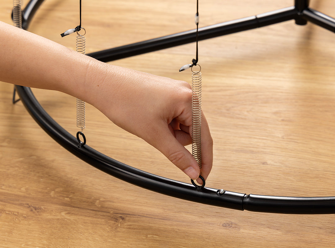 Close-up of hand attaching spring tension wire to the circular base ring of the Christow Snowfall LED Maypole Christmas Tree during assembly